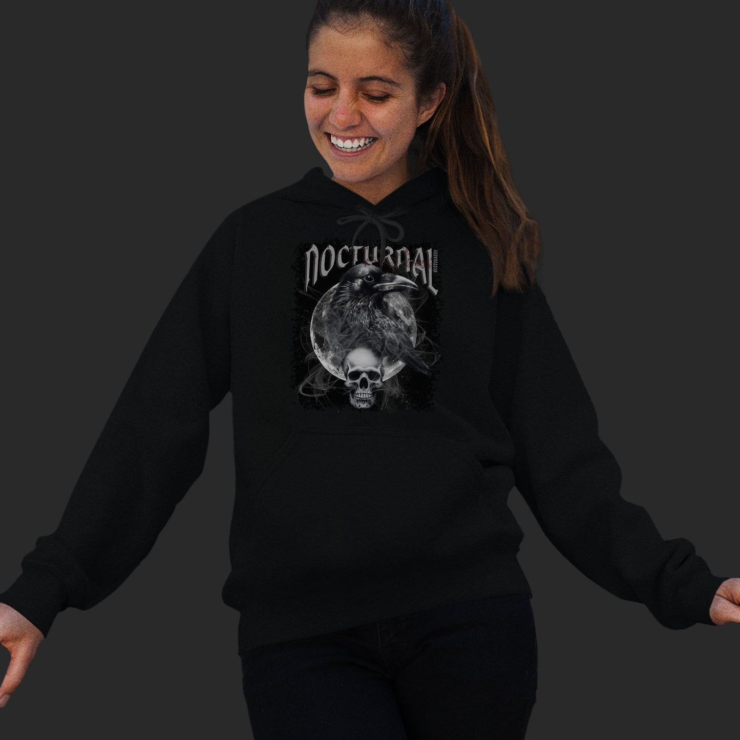 Woman Wearing A Black hoodie With An Illustration Of A Raven And Skeleton At Night Time With A Skull Under Full Moon